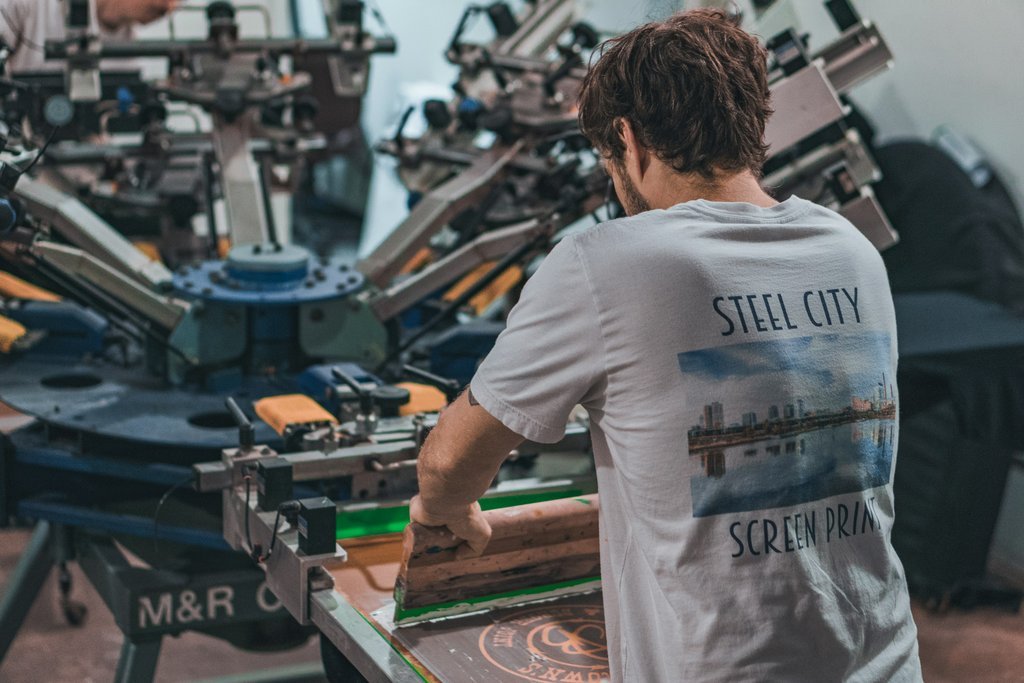 A man in a black hoodie reads by an industrial printing machine in Benghazi, Libya.