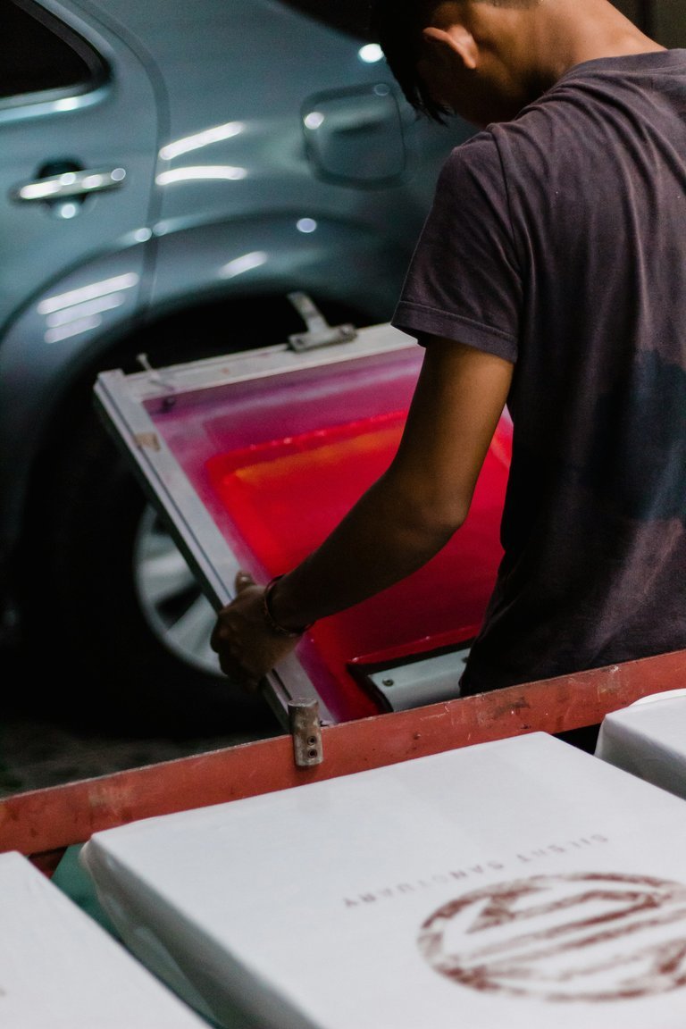 Person holding papers near a printing press in a workshop setting.